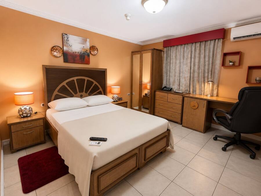 A hotel room with a bed, bedside tables, a desk with a chair, a wardrobe, and a window with curtains.