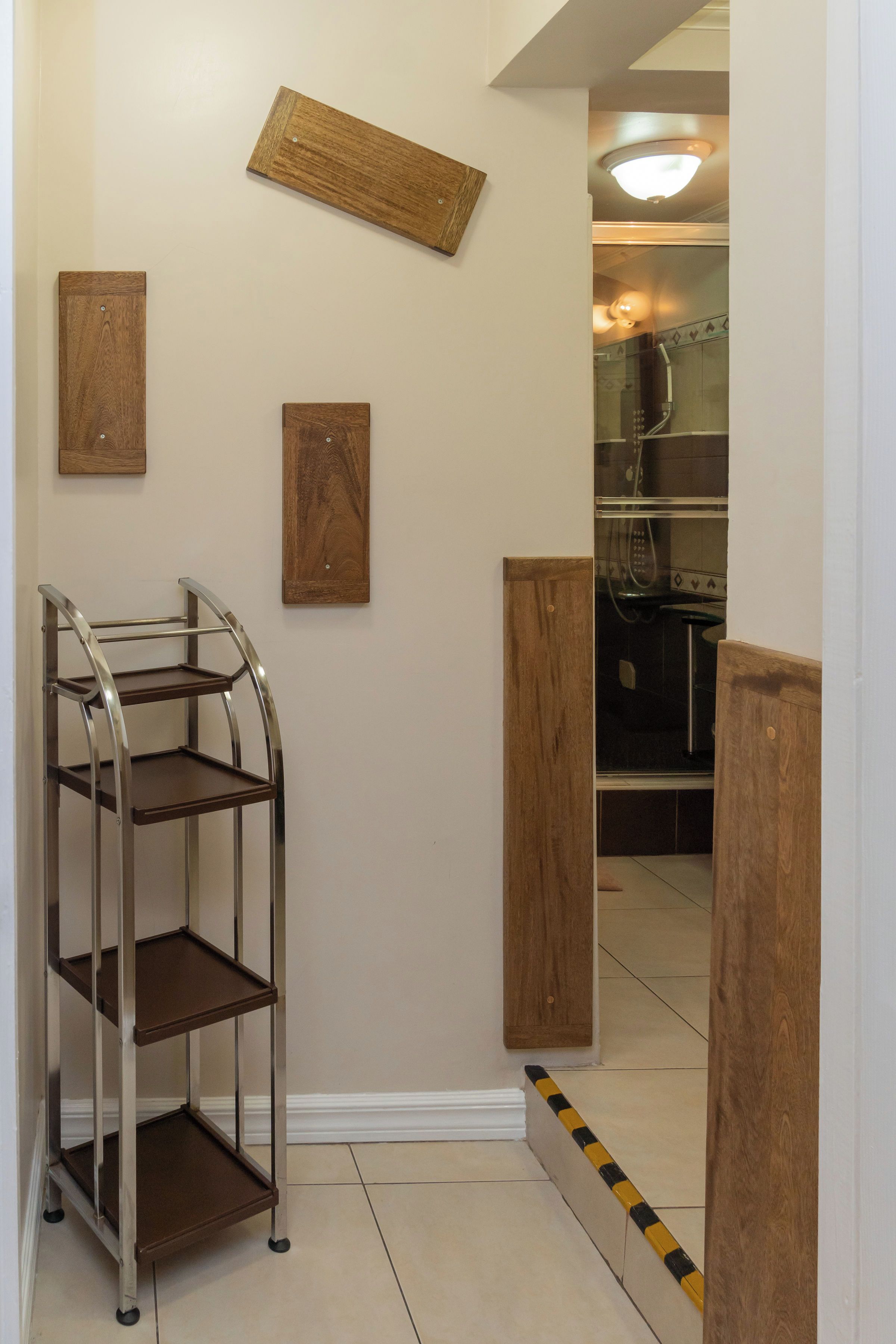 A hallway with a metal shelf unit, wooden wall decor, and a glimpse of a kitchen area.