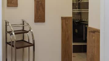 A hallway with a metal shelf unit, wooden wall decor, and a glimpse of a kitchen area.