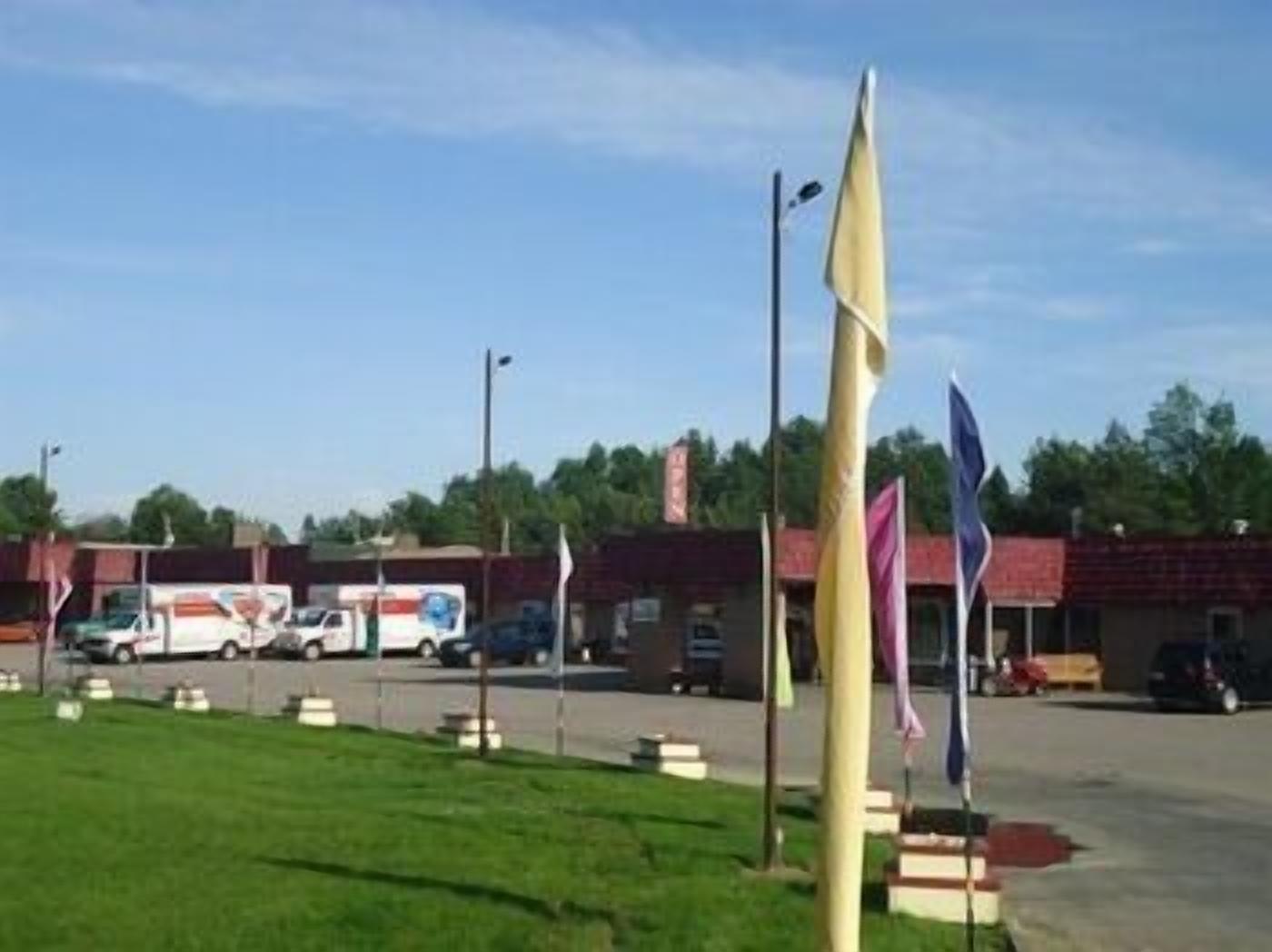A parking lot with several flags, a building with a red roof, and a white van in the background.