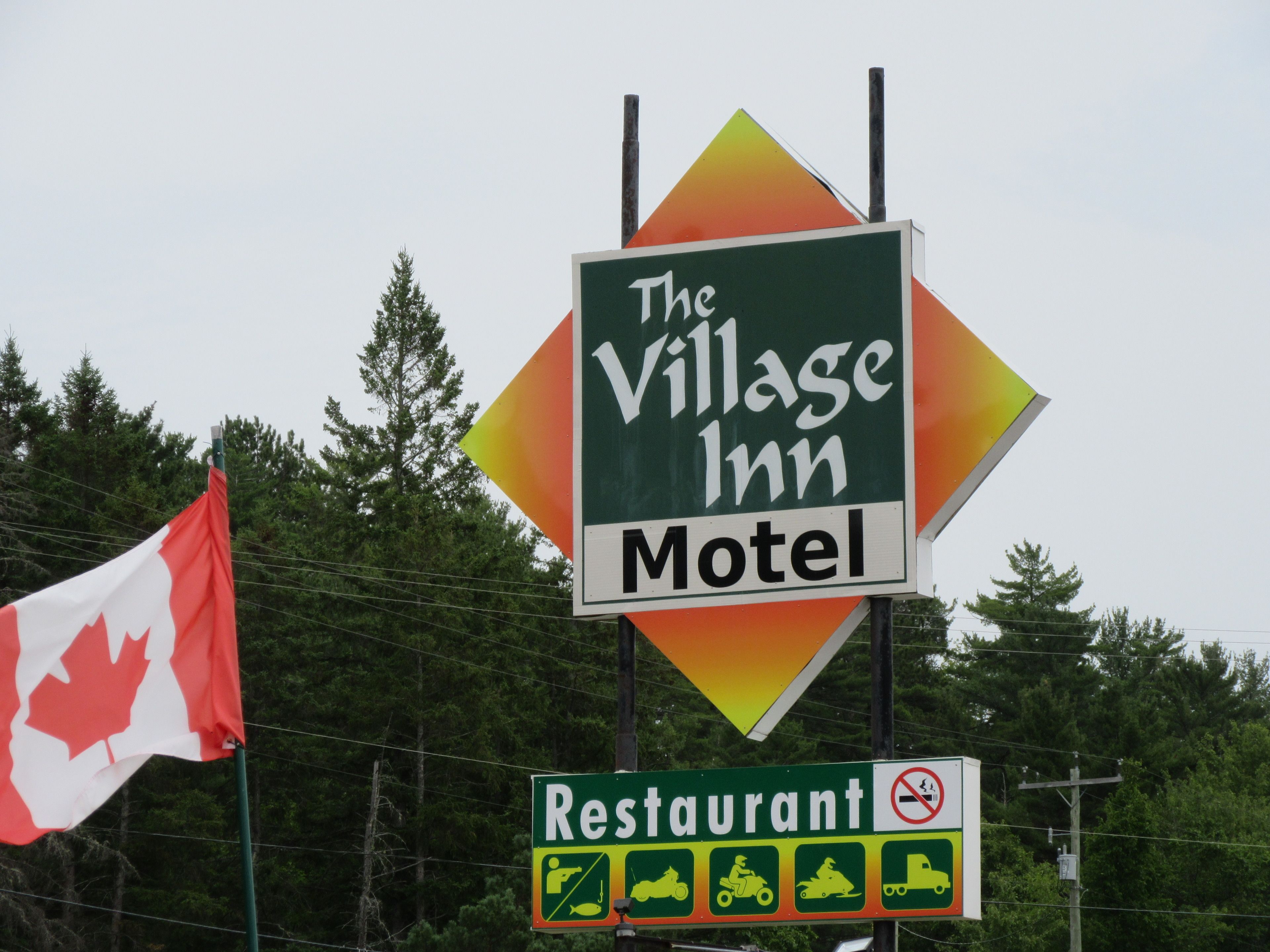 Un letrero del Motel y Restaurante Village Inn, con una bandera canadiense.