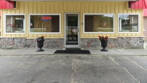 A yellow building with a red awning, a glass door, and a neon 'OPEN' sign. - The Village Inn Motel (Huron Shores)