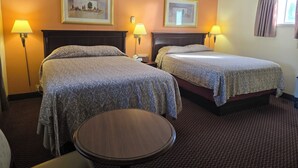 A hotel room with two beds, a round table, and two wall-mounted lamps. - The Village Inn Motel (Huron Shores)