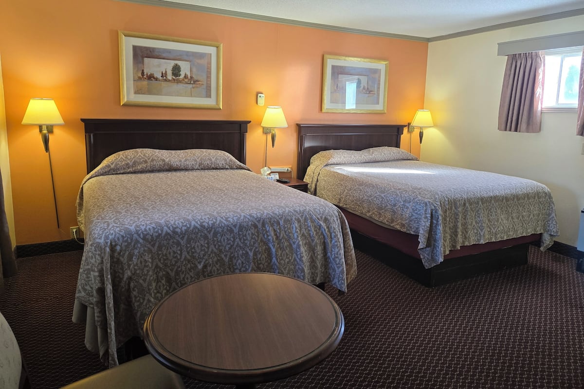A hotel room with two beds, a round table, and two wall-mounted lamps.