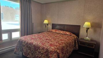 A hotel room with a large bed, two bedside lamps, a nightstand, and a window with curtains.