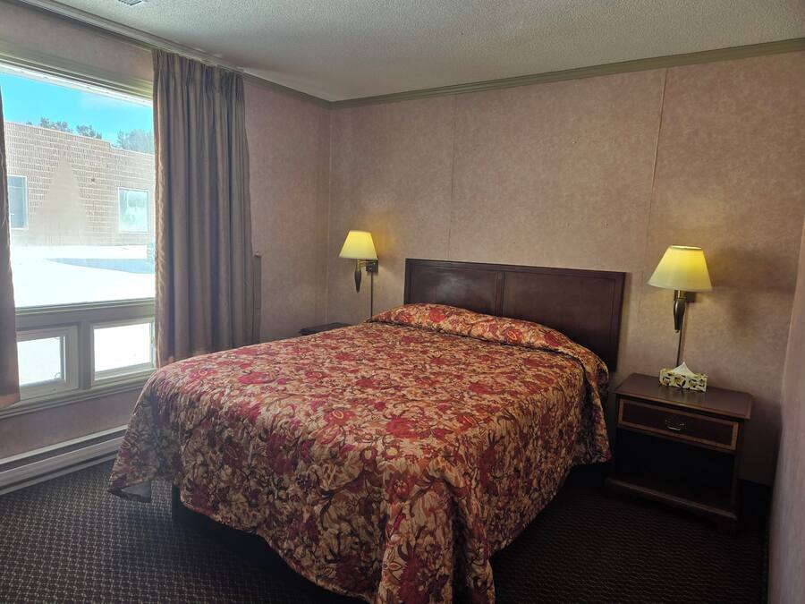 A hotel room with a large bed, two bedside lamps, a nightstand, and a window with curtains.