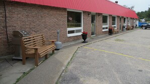 A brick building with a red roof, a bench, and a barbecue grill outside. - The Village Inn Motel (Huron Shores)