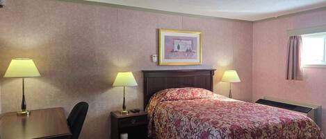 Habitación de hotel con una cama, dos lámparas de noche, un escritorio con una silla, una mesita de noche, un cuadro en la pared y una ventana con cortinas.