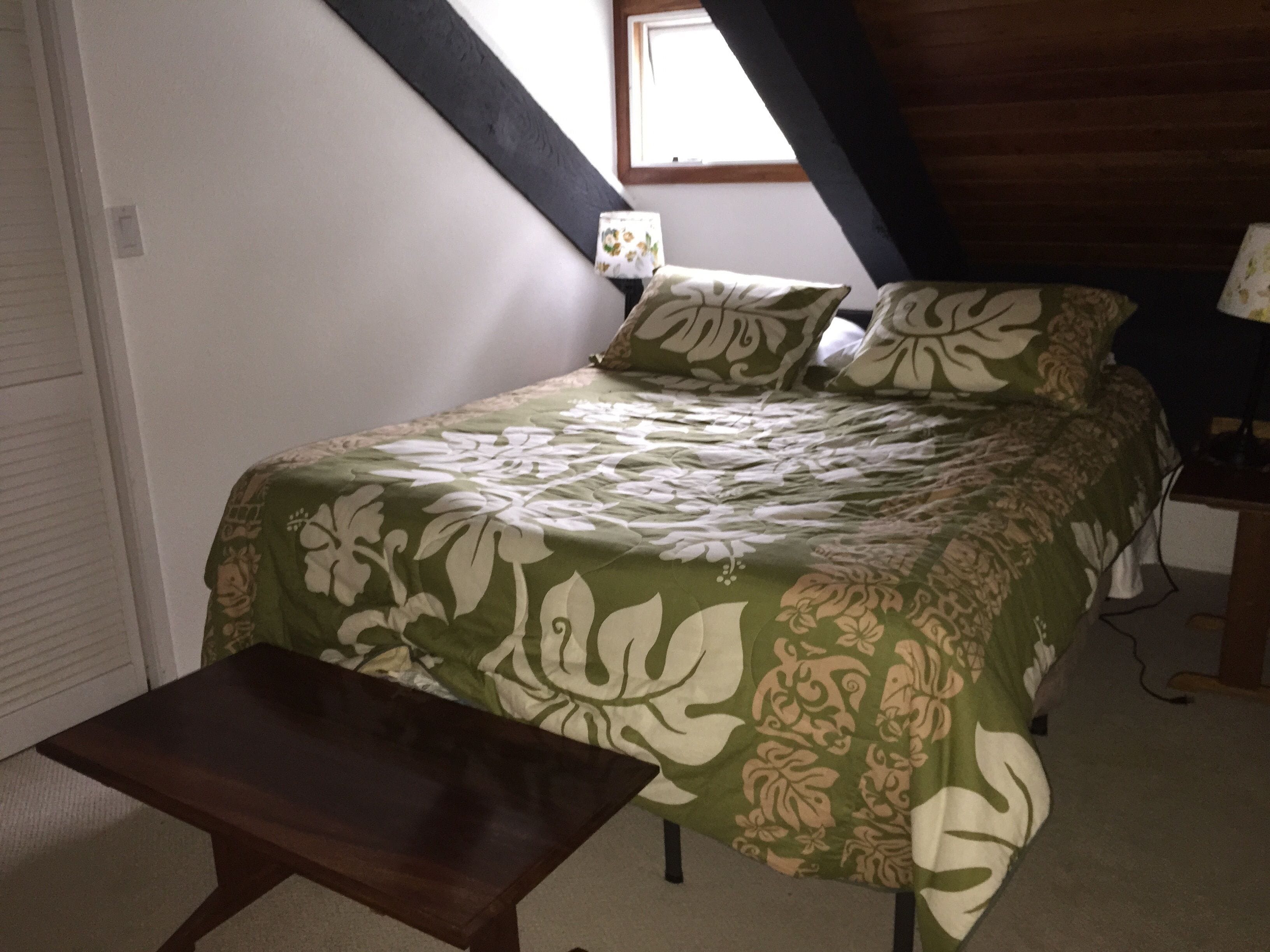A bedroom with a bed, a bench, a window, and a nightstand.