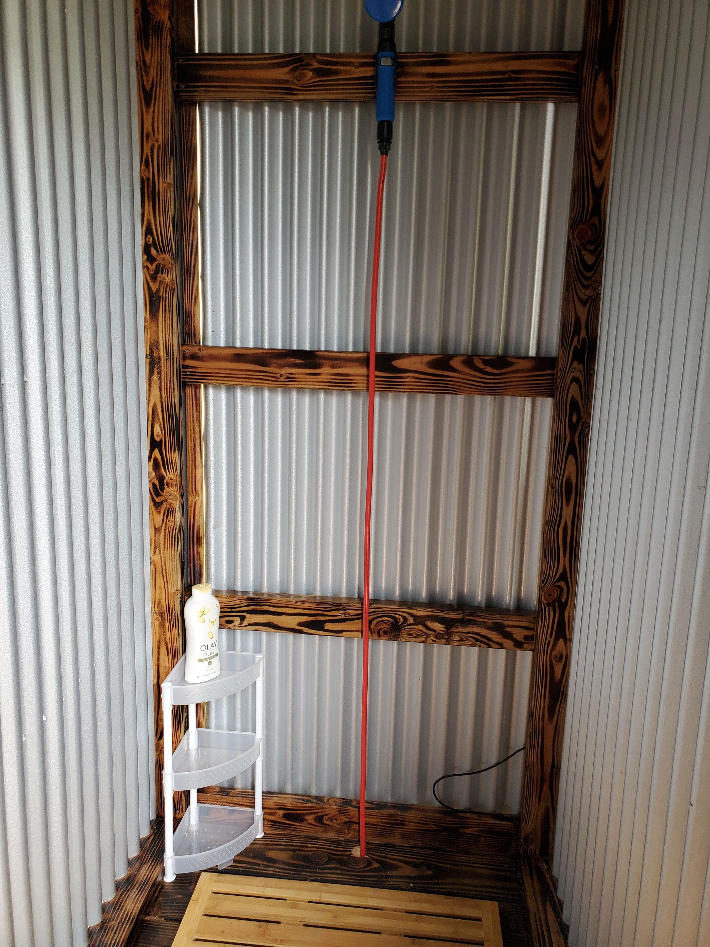Una habitación con ventana de madera, estante blanco con una botella y un cable de extensión rojo.