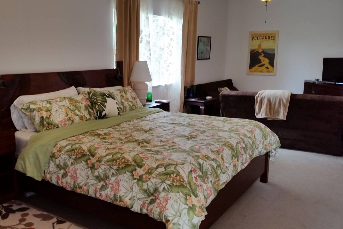 A bedroom with a floral bedspread, a wooden headboard, a nightstand with a lamp, a dresser, and a poster on the wall.