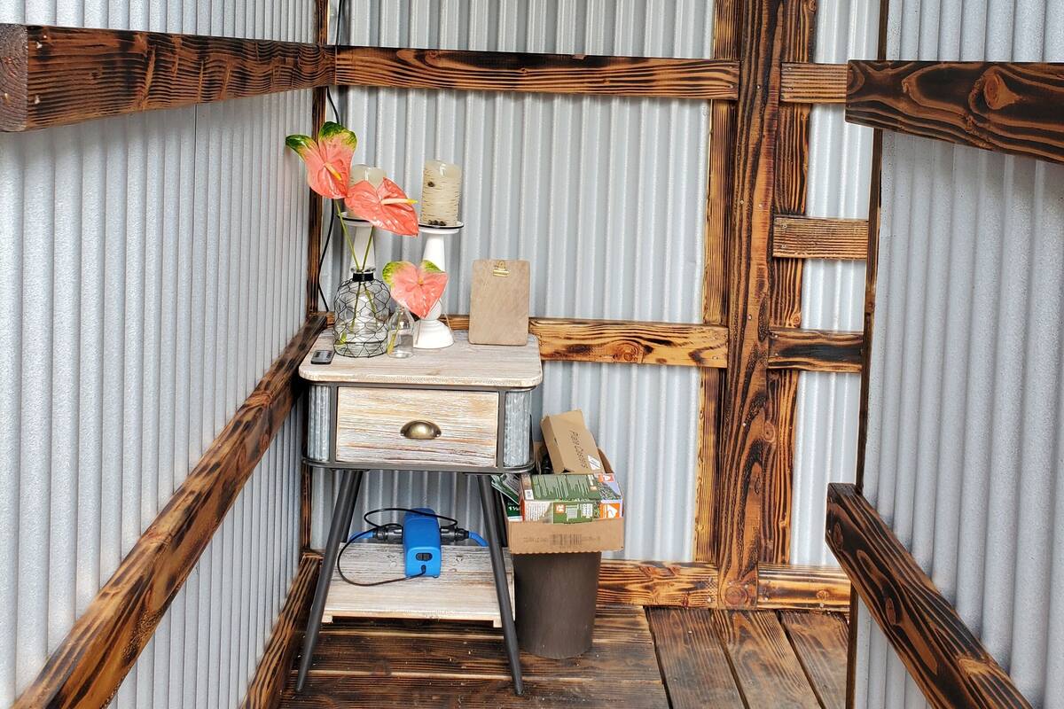 A compact room with a wooden desk, a small shelf with a speaker, and a trash bin.