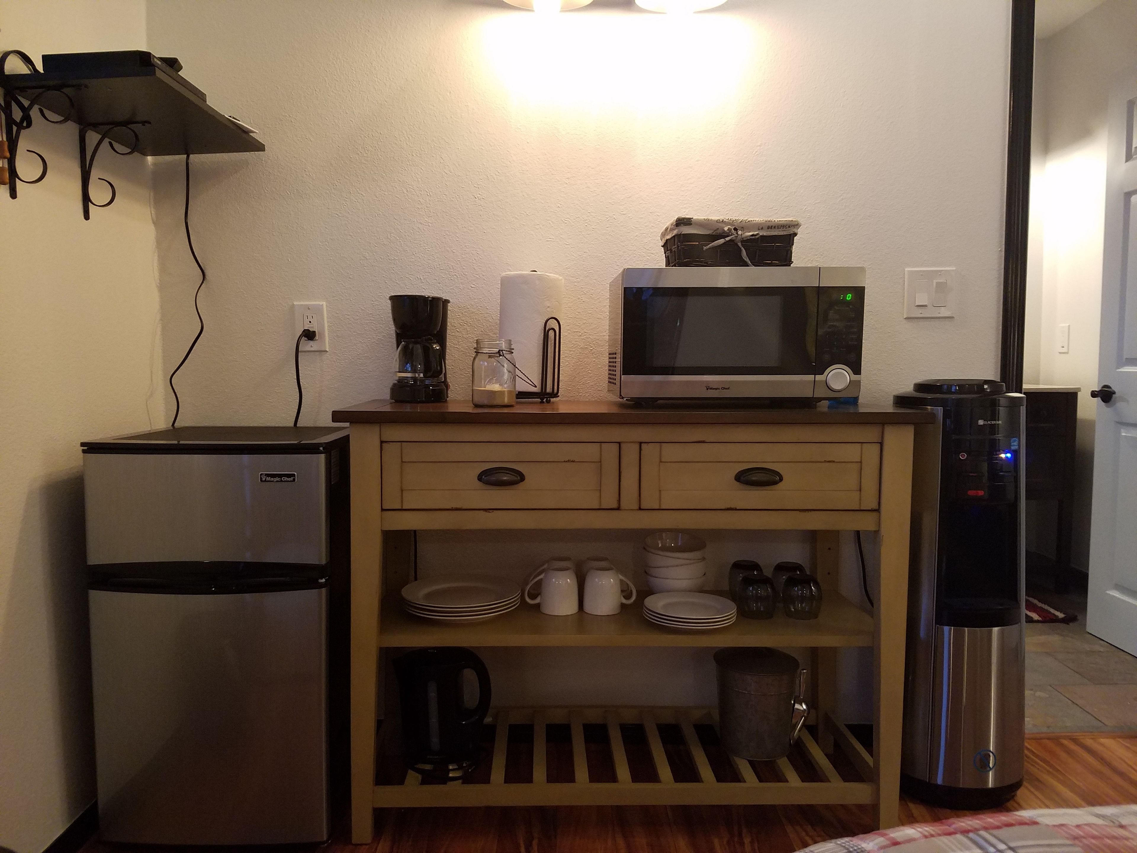 A compact kitchen with a refrigerator, microwave, coffee maker, and a water dispenser.