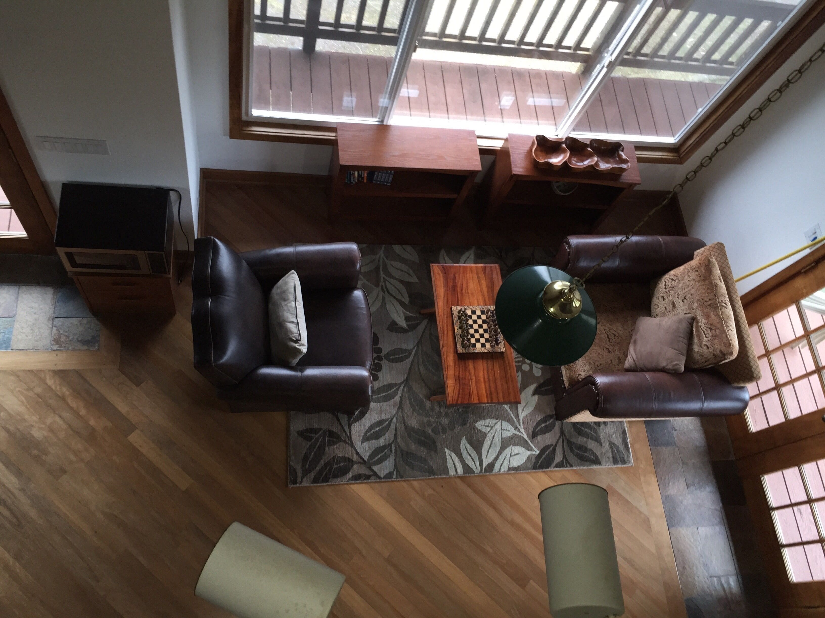 Ein großzügiger Wohnraum mit hoher Decke, Holzboden, einem braunen Ledersofa, einem passenden Sessel, einem Couchtisch und Blick durch große Fenster.