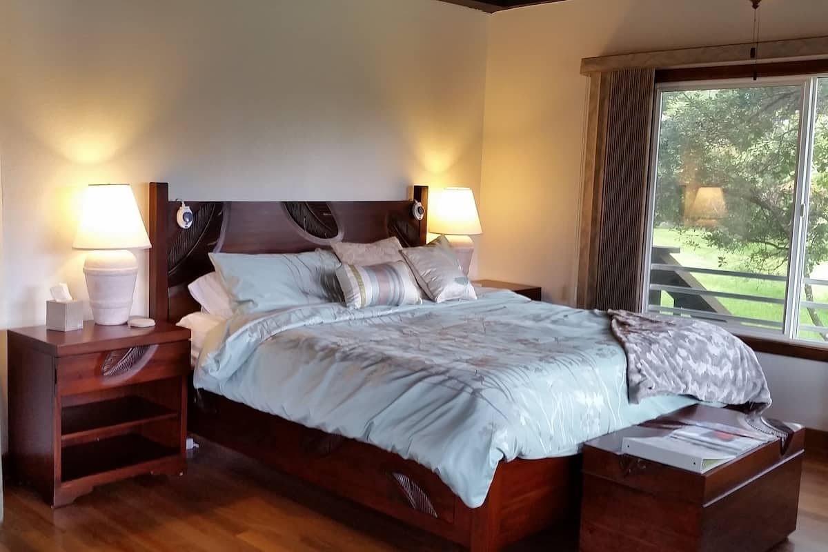 A neatly made bed with a wooden headboard, two bedside tables with lamps, and a window with curtains.