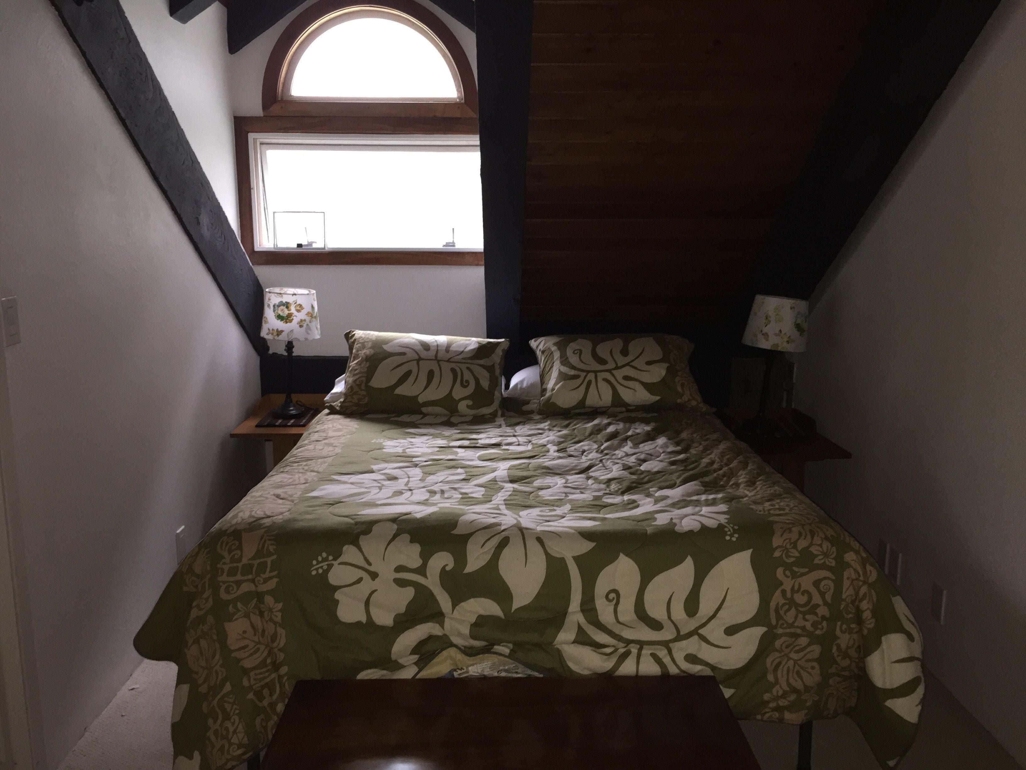A bedroom with a bed, two bedside tables, a window, and a small skylight.