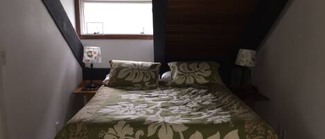 A bedroom with a bed, two bedside tables, a window, and a small skylight.