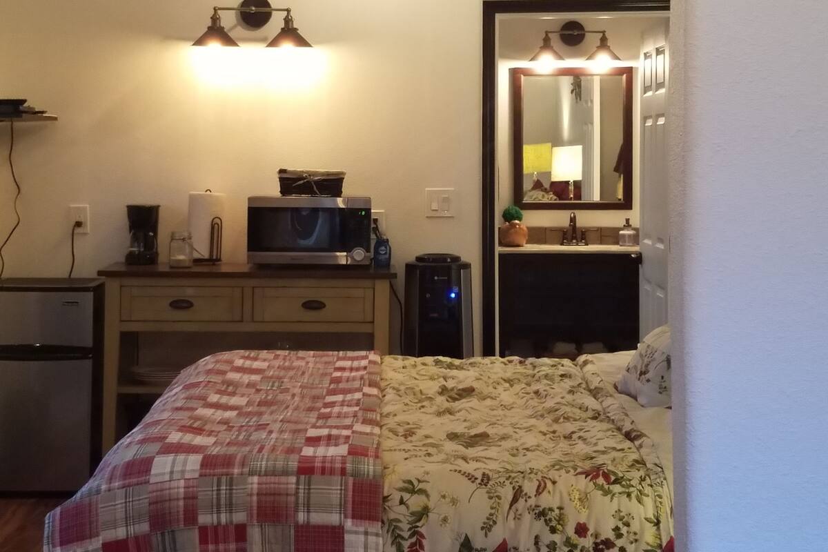 A hotel room with a bed, a desk with a computer, a ceiling fan, and a mirror.