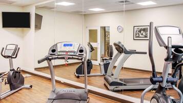 Un gimnasio con cintas de correr, elípticas y un espejo grande.