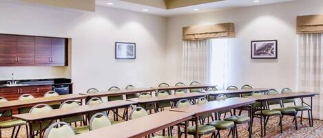 A conference room with long tables and chairs, a kitchenette, and framed pictures on the walls.