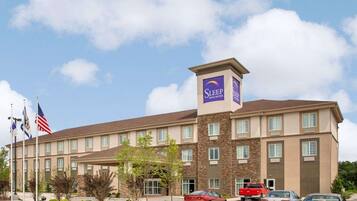 A Sleep Inn & Suites hotel with a central tower, multiple windows, and a parking lot with cars.