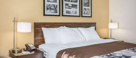 Una habitación de hotel con una cama, mesitas de noche, una lámpara, un teléfono y cuadros en la pared.
