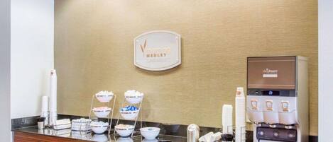 A hotel reception area with a coffee machine, a sign reading "Morning Medley," and a counter with bowls of food.