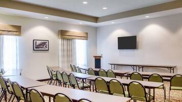 A conference room with multiple tables and chairs, a flat-screen TV mounted on the wall, and a podium.