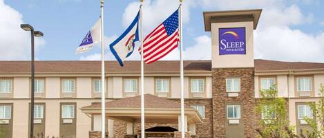 A Sleep Inn & Suites hotel with a stone facade, multiple flags, and a clear sky.