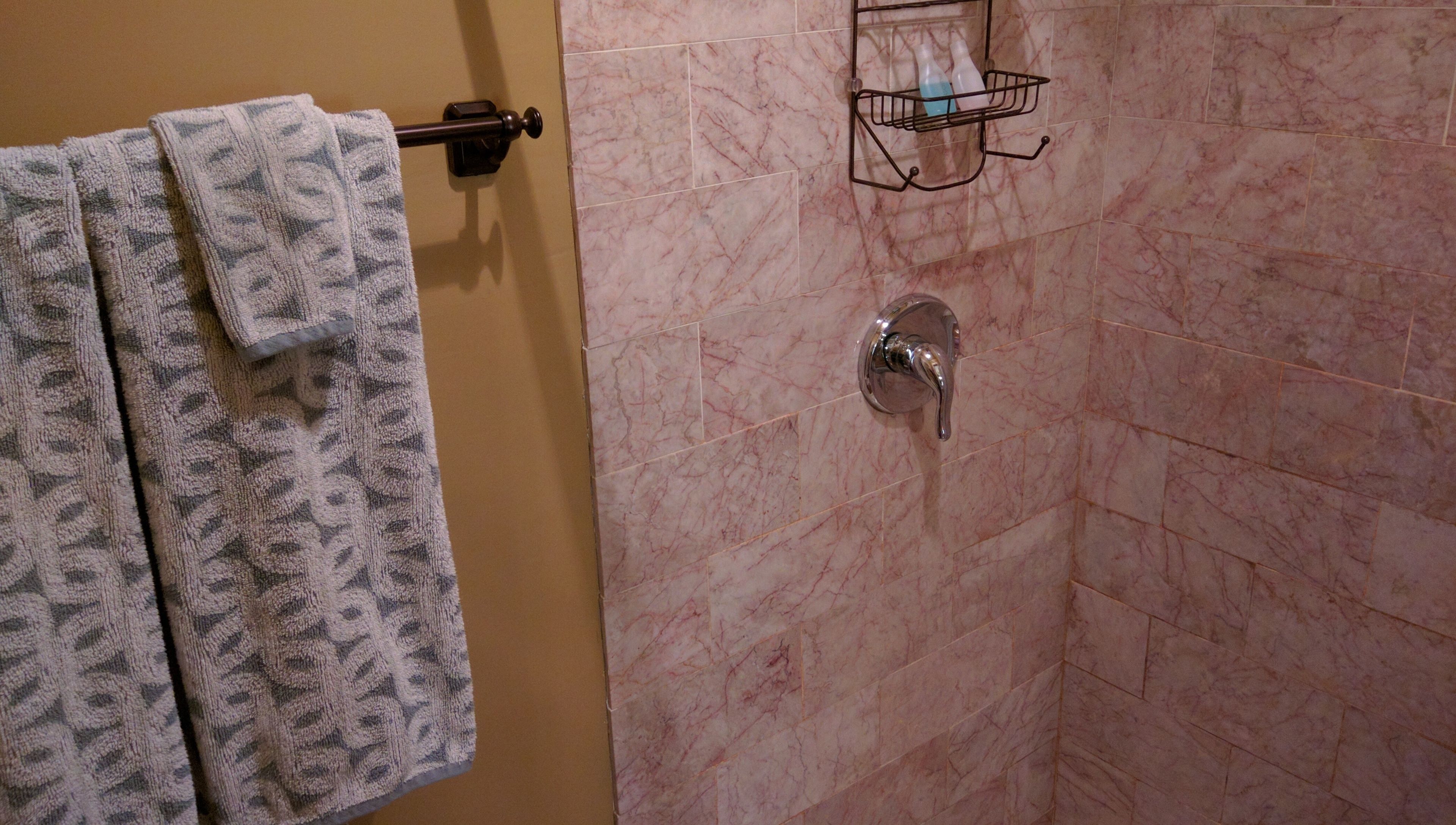 A bathroom with a towel rack holding two patterned towels, a shower with a chrome faucet, and a soap dish on the wall.