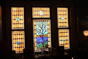 A stained glass window with a tree and landscape design, framed by wooden panels.