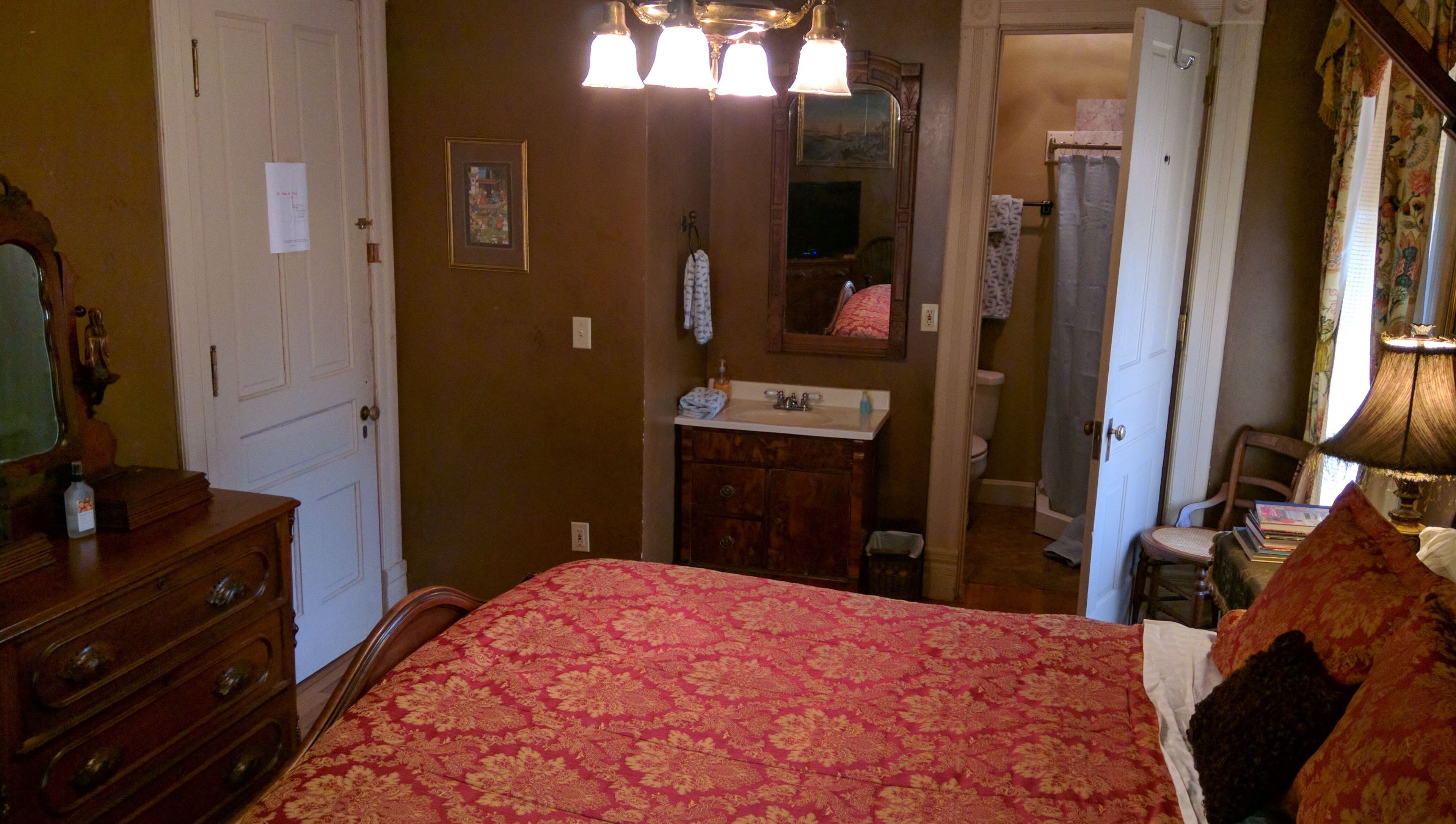 A bedroom with a bed, dresser, and a bathroom visible through an open door.
