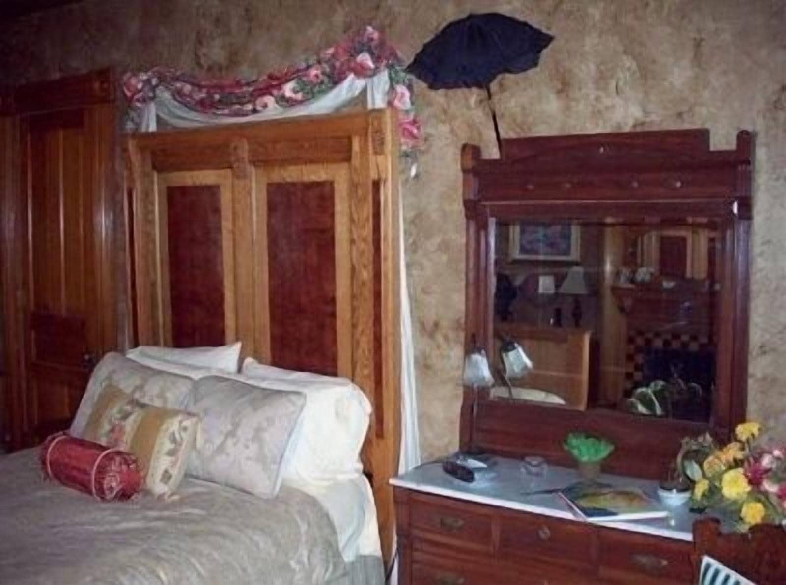 A bedroom with a wooden bed, a dresser, a mirror, and a floral arrangement.