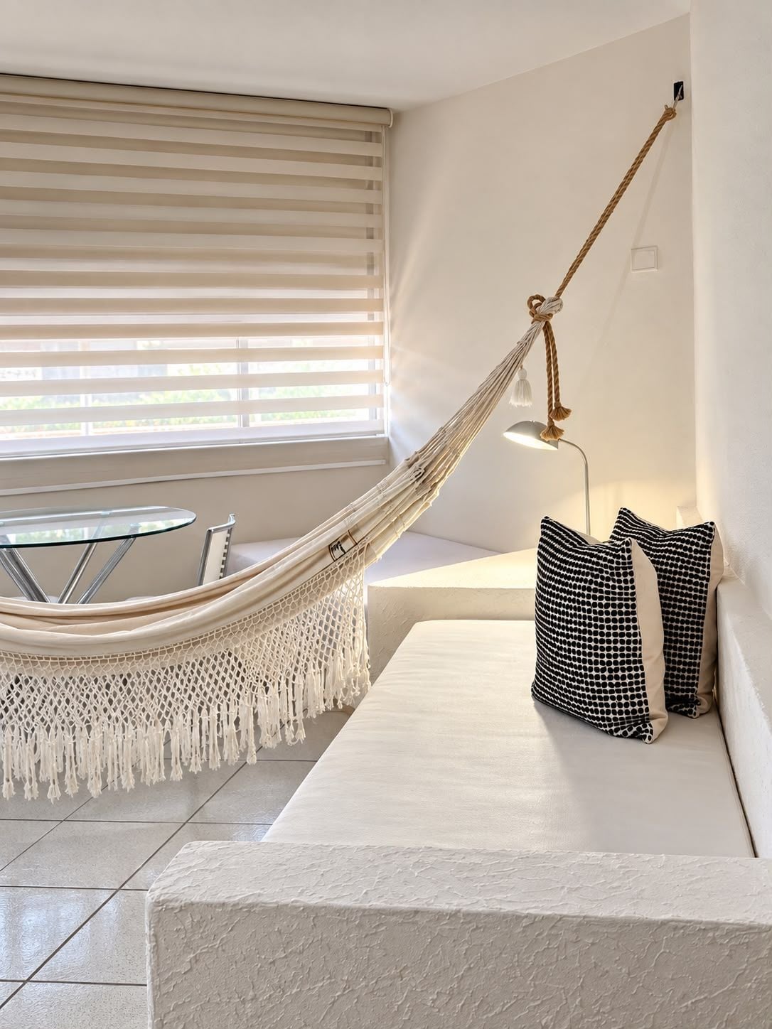 A hammock suspended from a ceiling, a round table with chairs, a sofa with patterned cushions, and a hanging lamp.