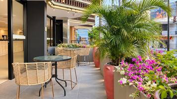 An outdoor seating area with wicker chairs and a glass table, surrounded by potted plants and flowers.