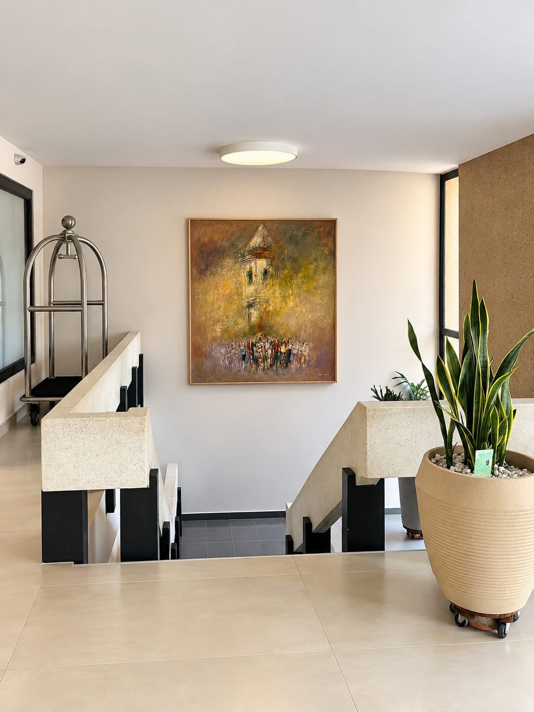 A modern lobby with a staircase, a large abstract painting, and a potted plant.