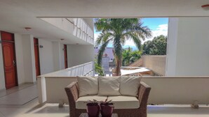 A balcony with a wicker sofa, two potted plants, and a view of palm trees and buildings. - Hotel Sicarare (Valledupar)