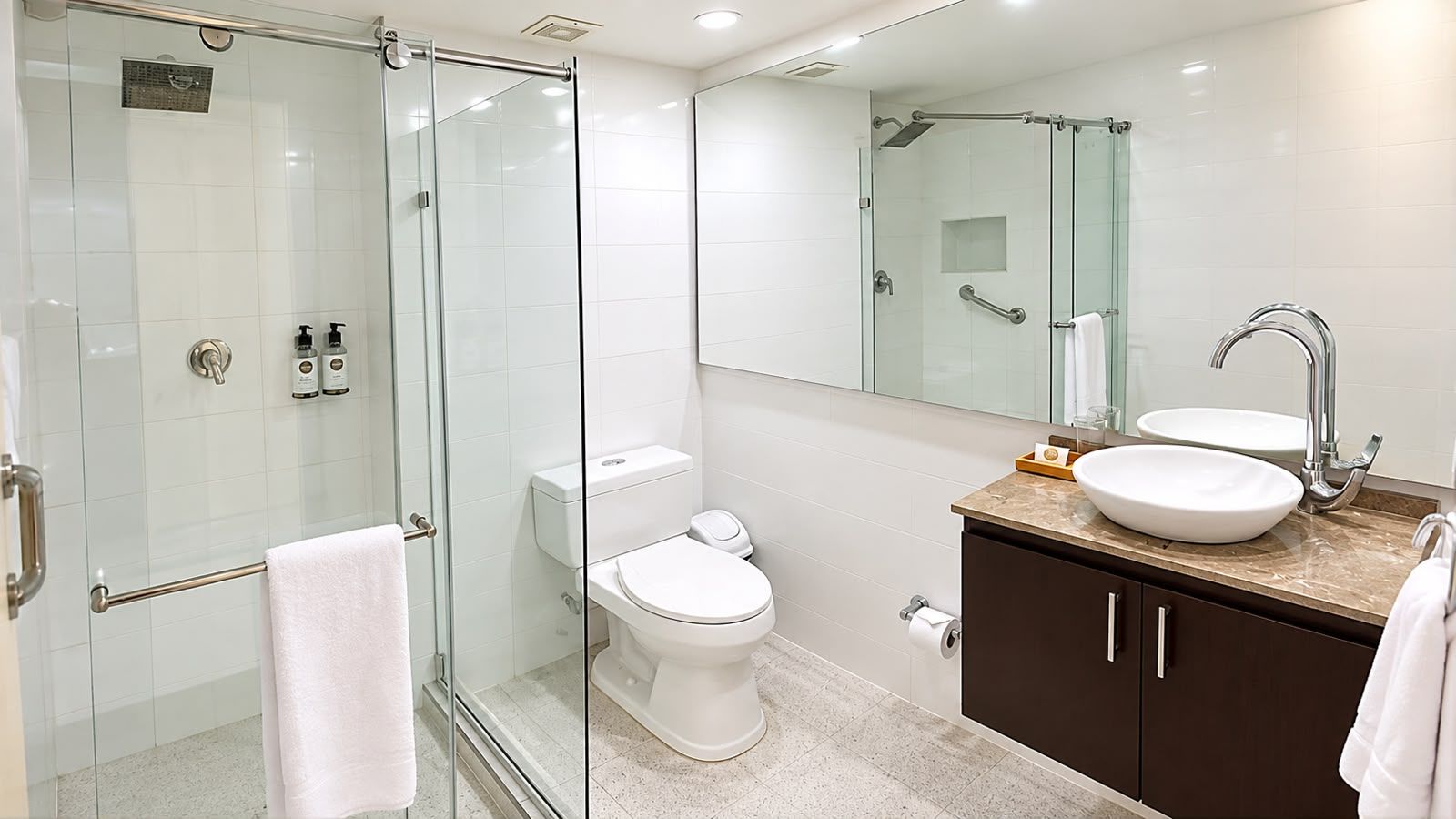 Une salle de bain moderne avec une douche à parois de verre, des toilettes, un lavabo avec un meuble-vasque et un grand miroir.