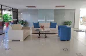 A modern living room with a beige sofa, a coffee table, and a blue armchair. There are potted plants and a glass partition with the word "solar" on it. - Hotel Sicarare (Valledupar)