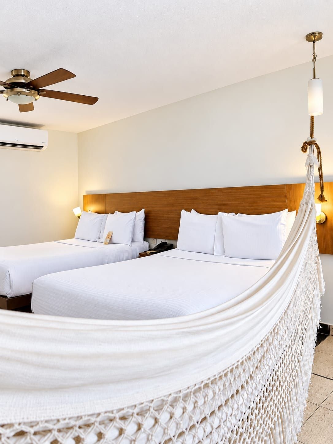 A hotel room with a bed, two bedside tables, a ceiling fan, and a wall-mounted air conditioning unit.