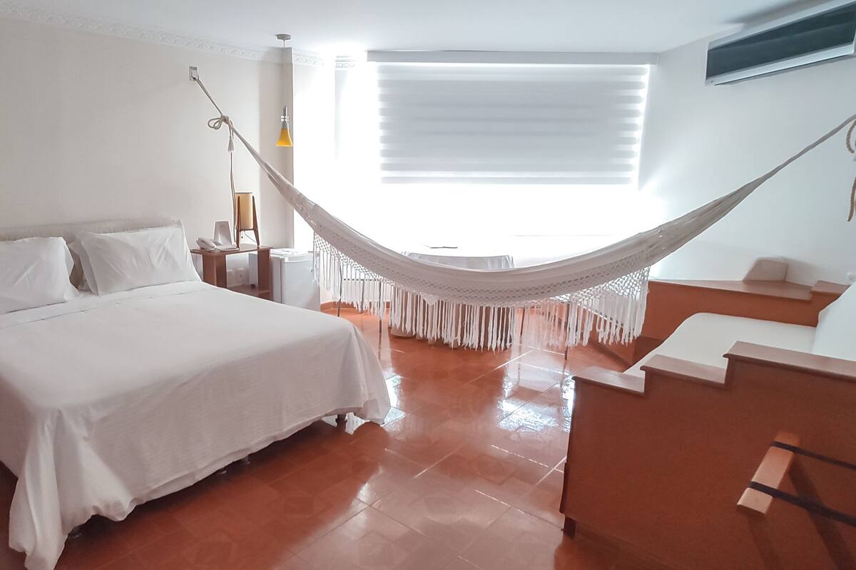 Ein Schlafzimmer mit Bett, Nachttischen, einer Lampe, einer Hängematte und einer Treppe.