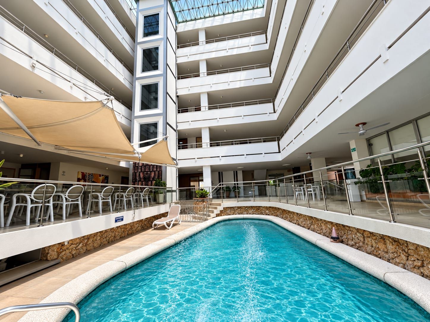 A multi-level indoor swimming pool with clear glass ceilings, multiple balconies, and a stone-lined pool edge.