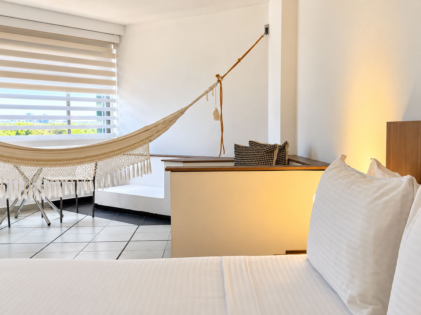 Une chambre d’hôtel moderne équipée d’un lit, d’un hamac, d’un bureau et offrant une vue sur la verdure environnante.