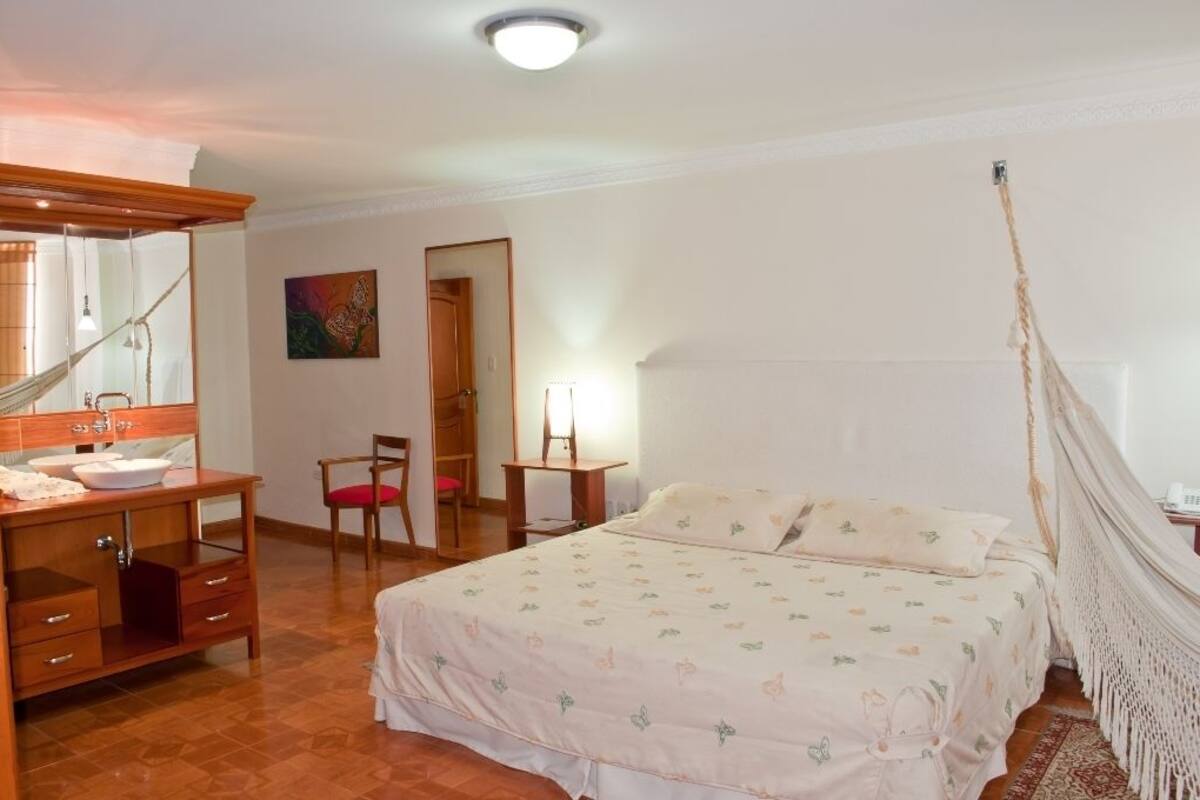 Ein Schlafzimmer mit einem Bett, einer hölzernen Kommode, einem Sessel, einem Nachttisch und einer Hängematte.