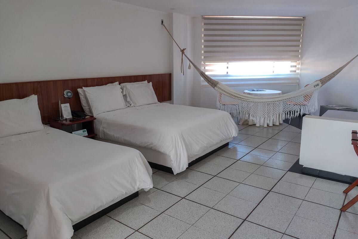 Ein Hotelzimmer mit zwei Betten, einem kleinen Tisch, einem Stuhl, einer Hängematte und einem Fenster mit Jalousien.