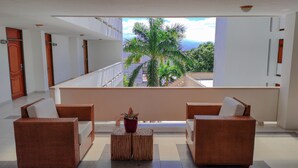 A balcony with wicker furniture, a potted plant, and a view of palm trees and buildings. - Hotel Sicarare (Valledupar)