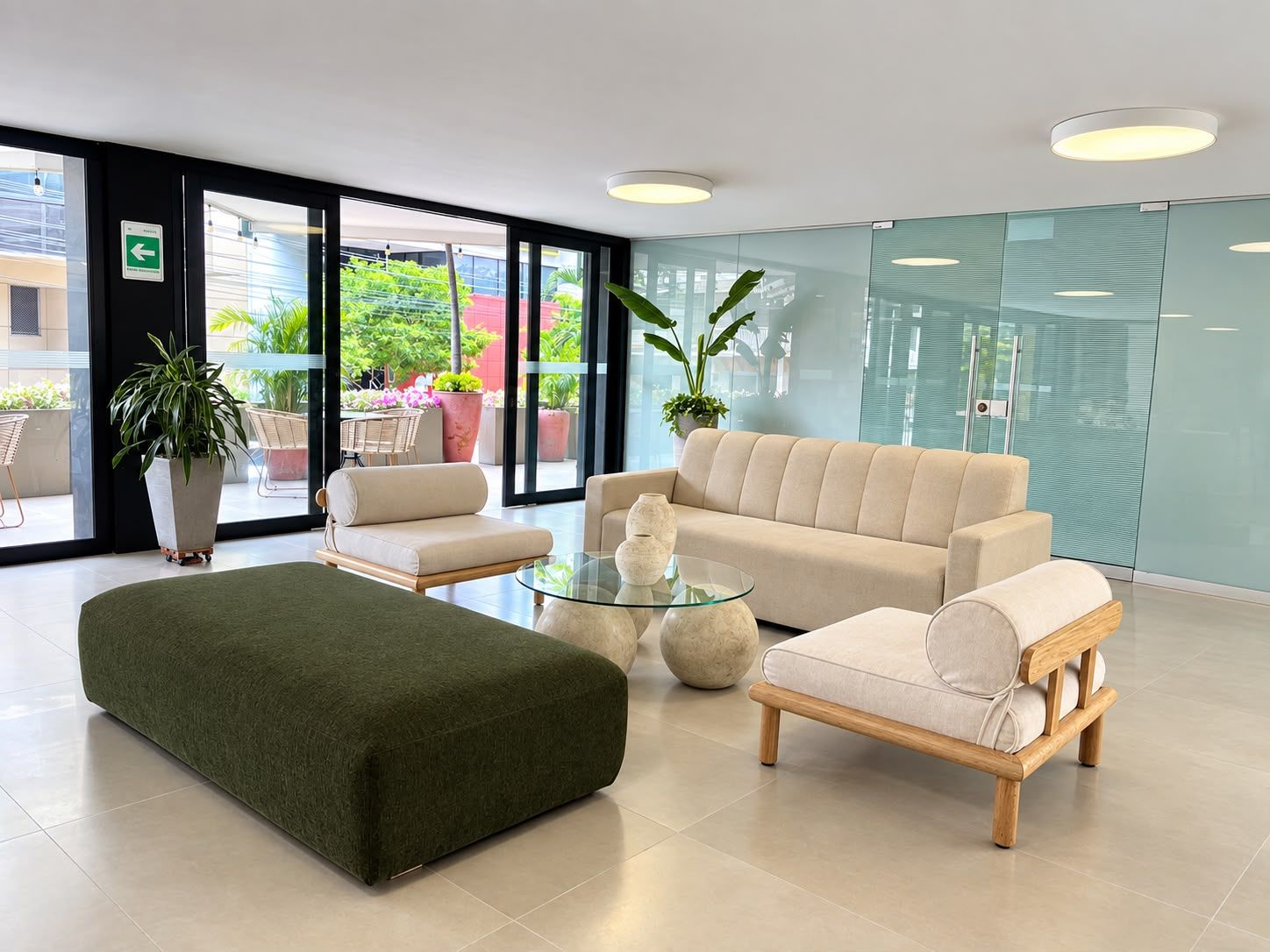 A modern lobby with a sofa, ottoman, and chairs, a glass coffee table, and potted plants.