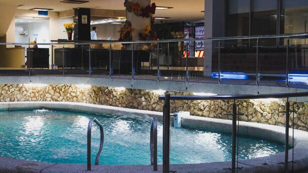 A swimming pool with a stone wall and metal railings, a reception area with a counter and chairs, and a ceiling fan. - Hotel Sicarare (Valledupar)