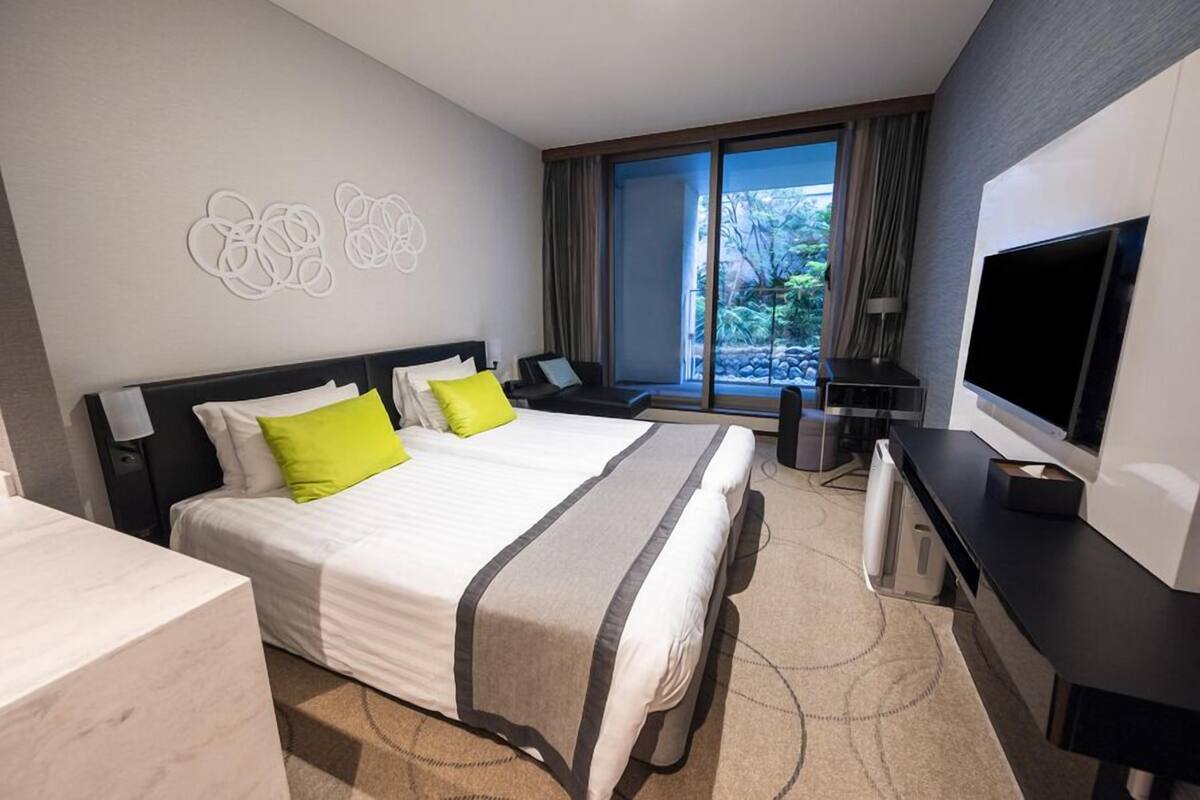 A hotel room with a bed, a desk, a television, and a view of the outdoors.