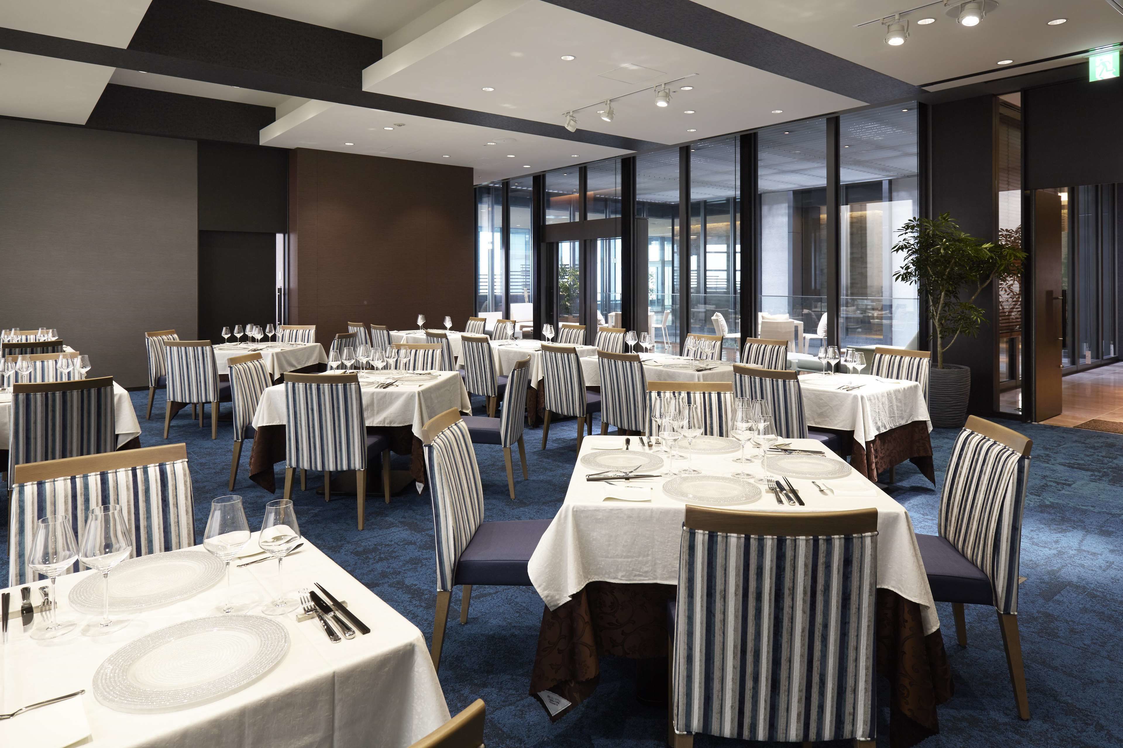 A modern dining area with multiple tables set for guests, featuring striped chairs and white tablecloths.
